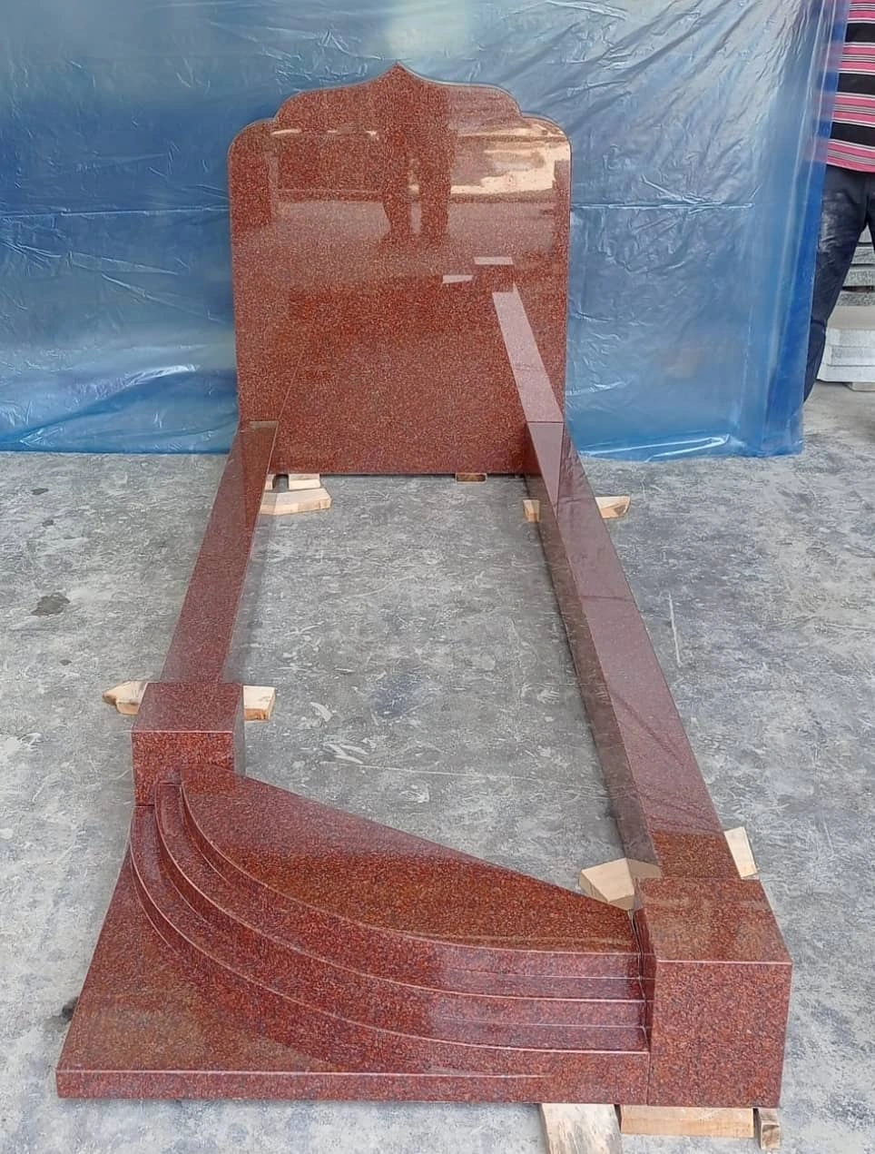 Red memorial with a shaped headstone and a curved, stepped foot, shown in the workshop.