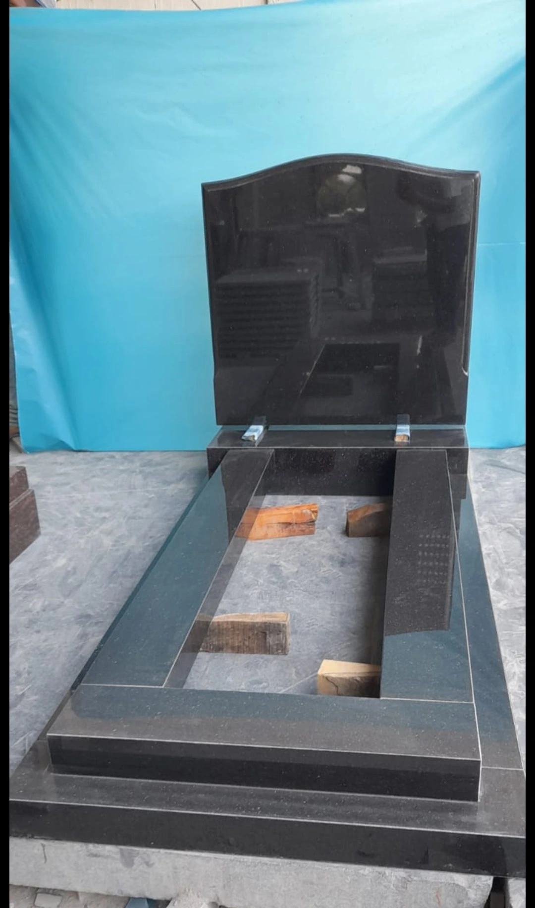 Black memorial with a gently arched headstone and stepped rectangular base, shown in the workshop.