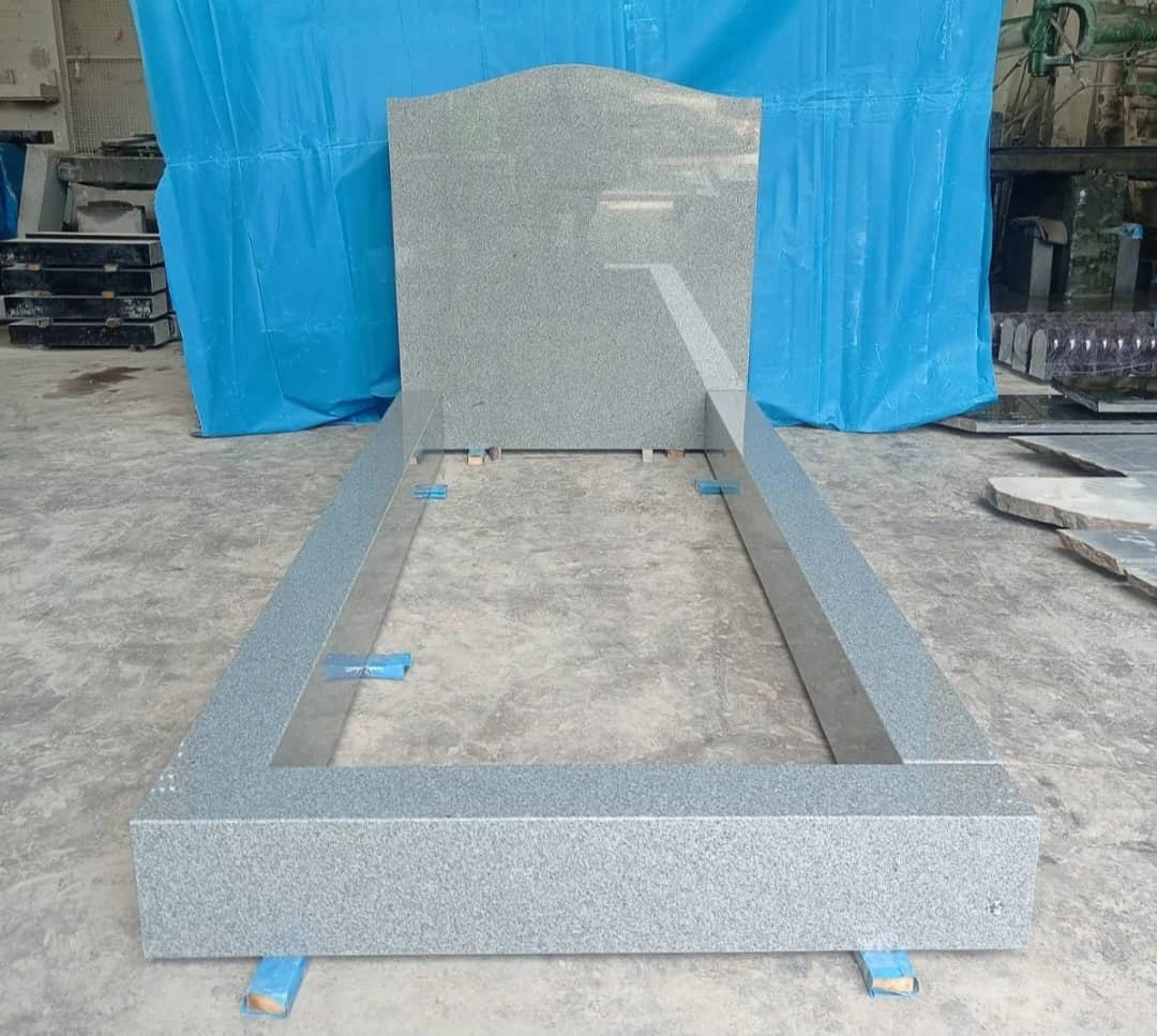 Light grey memorial with a shallow-arched headstone and straight rectangular kerb surround, shown in the workshop.