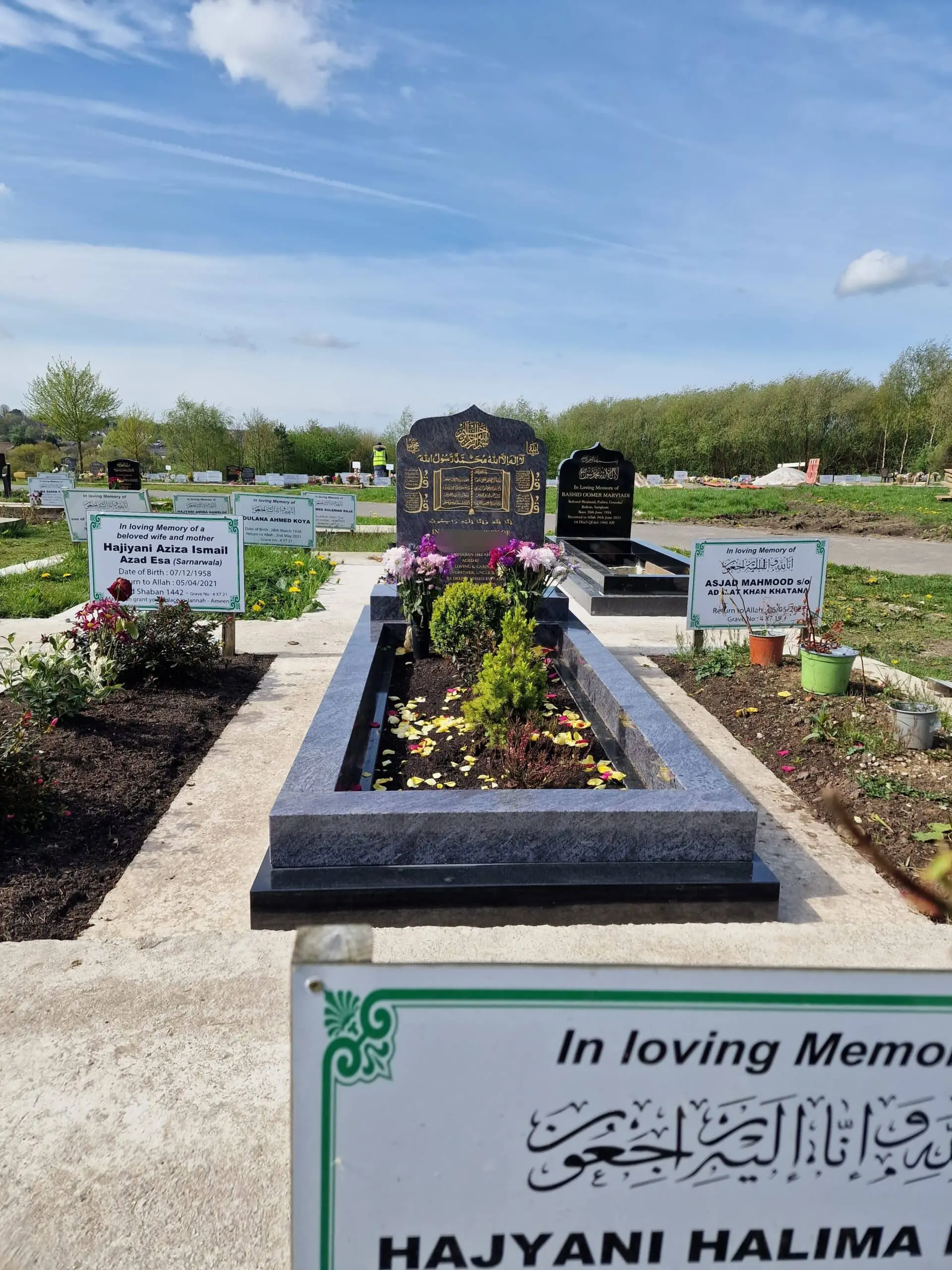 Grey memorial with a decorative shaped headstone, gold calligraphy and a full kerb surround containing flowers and planting